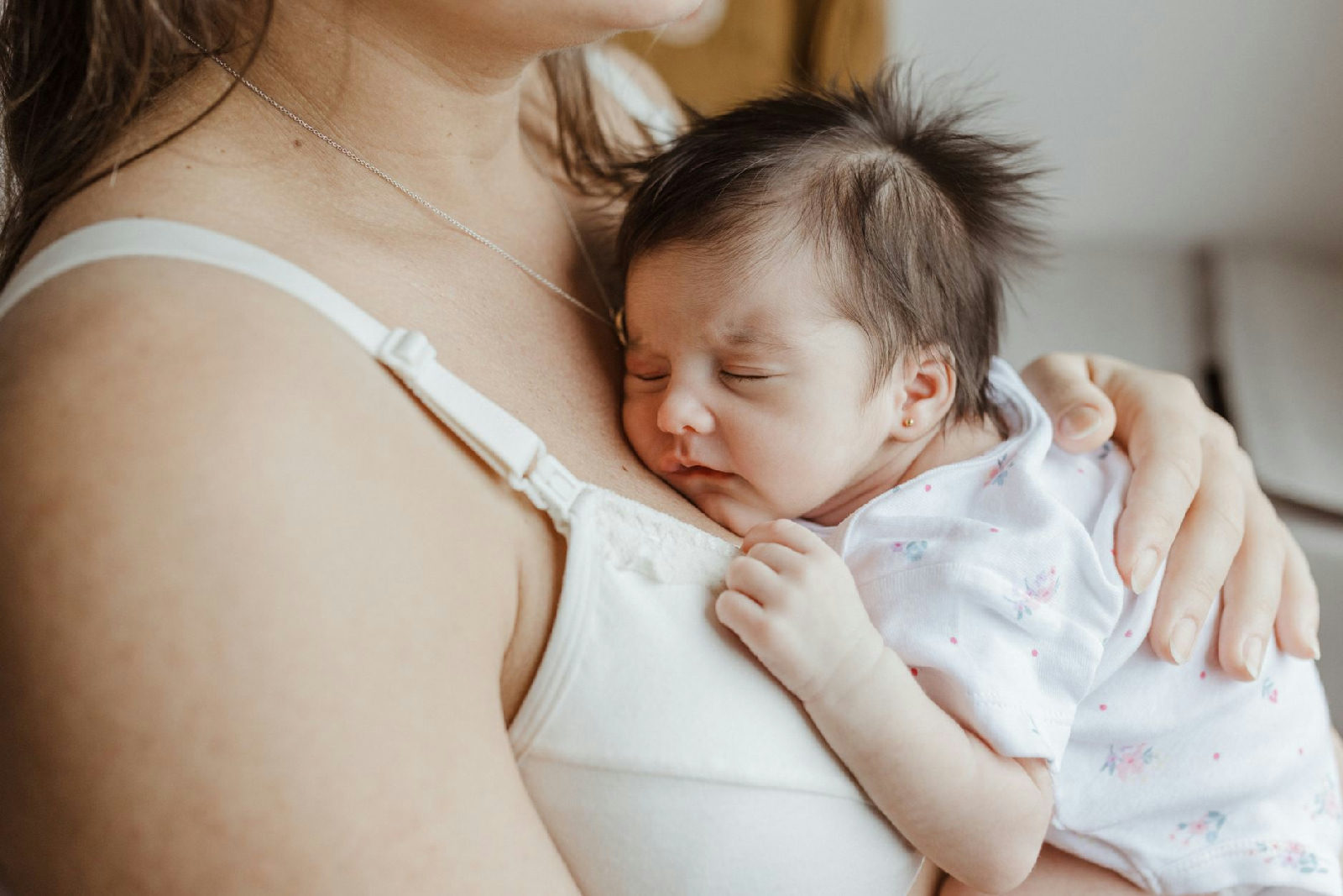 Mãe com expressão pensativa abraça seu bebê, ilustrando a complexidade emocional e a culpa materna na jornada da maternidade…