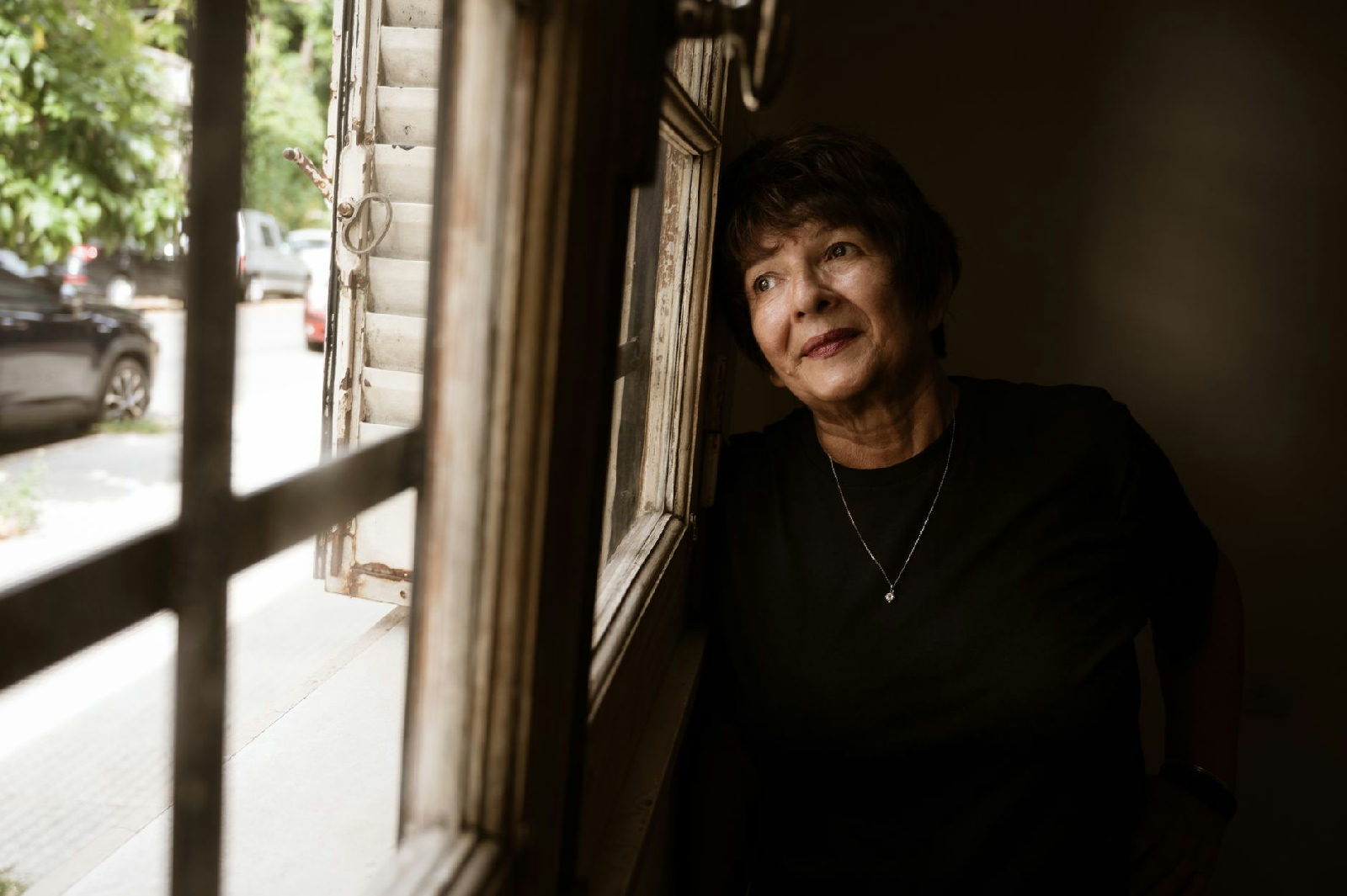 Mulher de meia-idade olhando pela janela em uma sala em Curitiba, refletindo sobre como lidar com a culpa no luto.