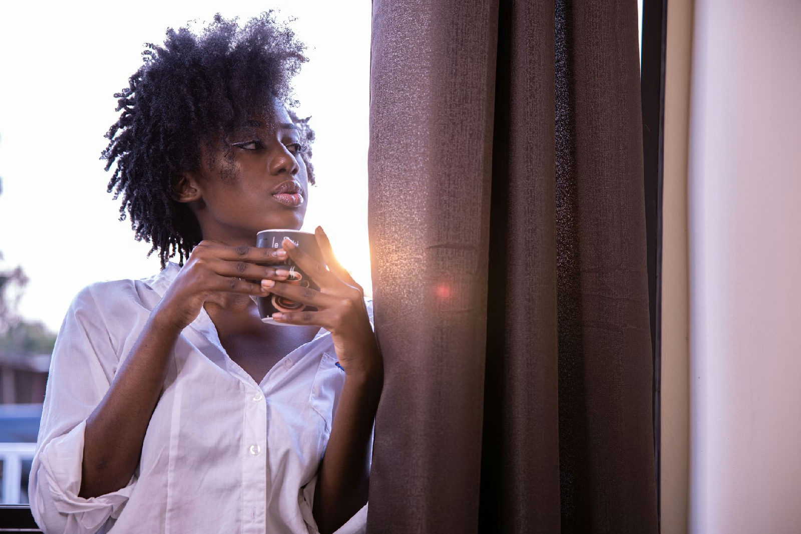 Mulher olhando pela janela com expressão de esperança, refletindo sobre como mudar hábitos com a ajuda de uma psicóloga em C…